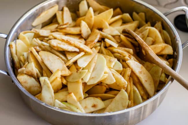 raw sliced apples in a pan with spices and flour and a wooden spoon.