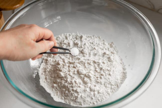 adding salt to a large bowl of bread flour.