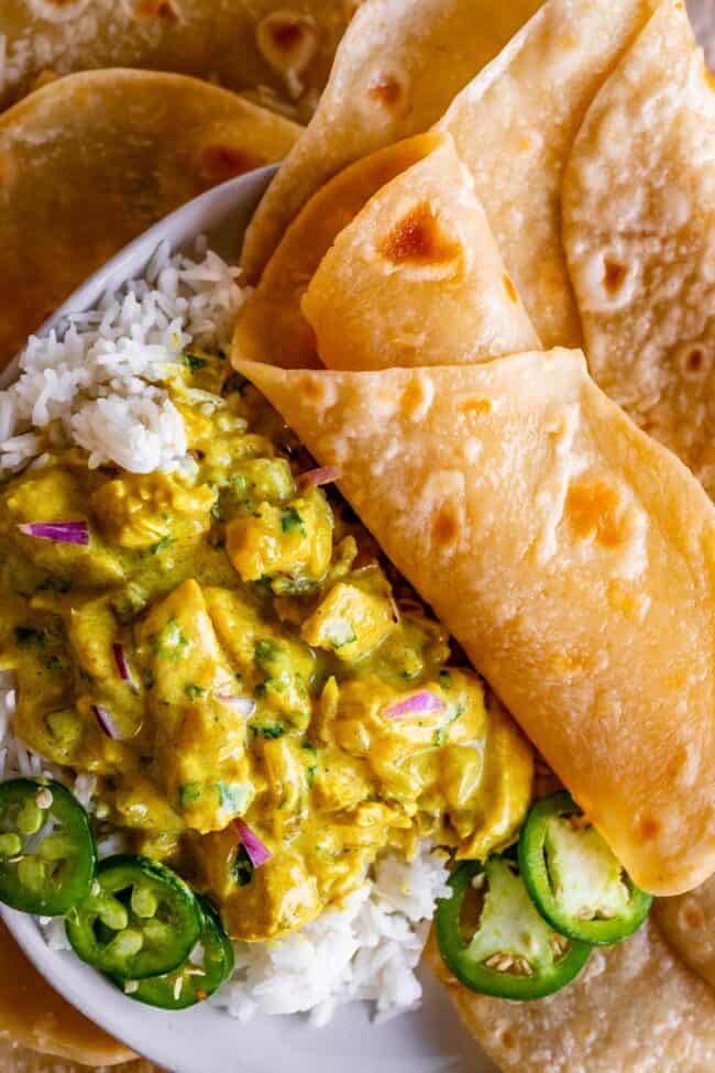 roti rolled up on a plate with curry and rice and jalapenos.