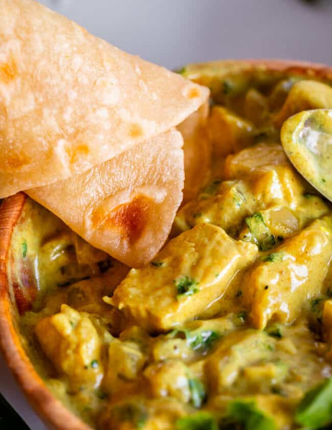 rolled Indian flatbread dipping into yellow curry.