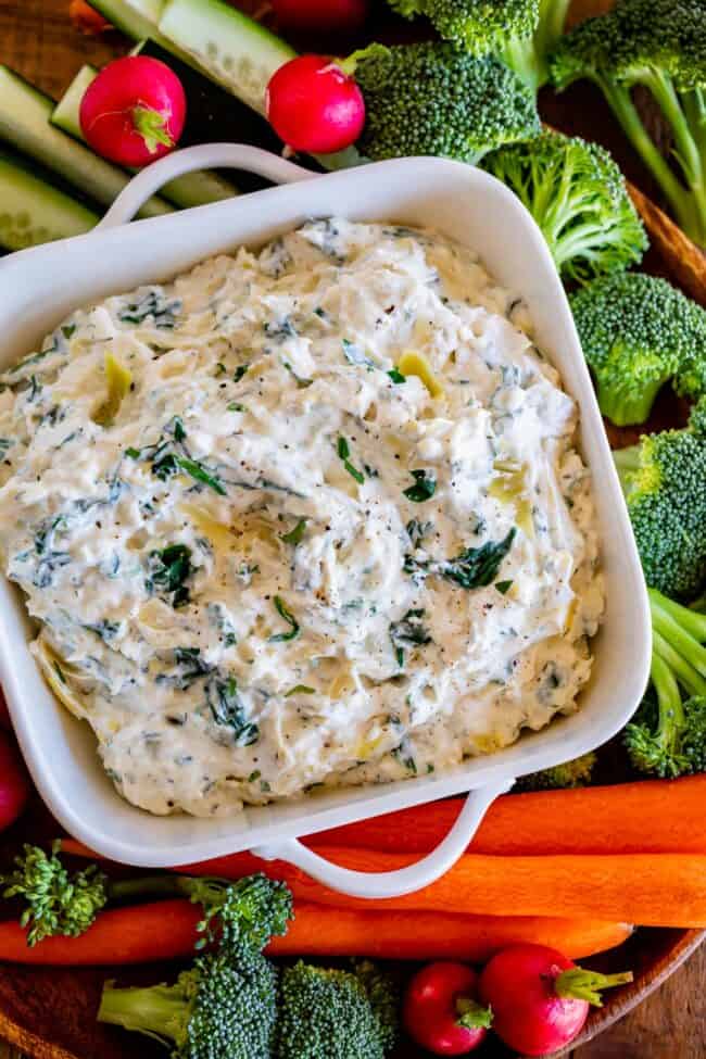 spinach artichoke dip in a white bowl surrounded by vegetables