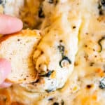 hand dipping bread into cheesy best spinach artichoke dip