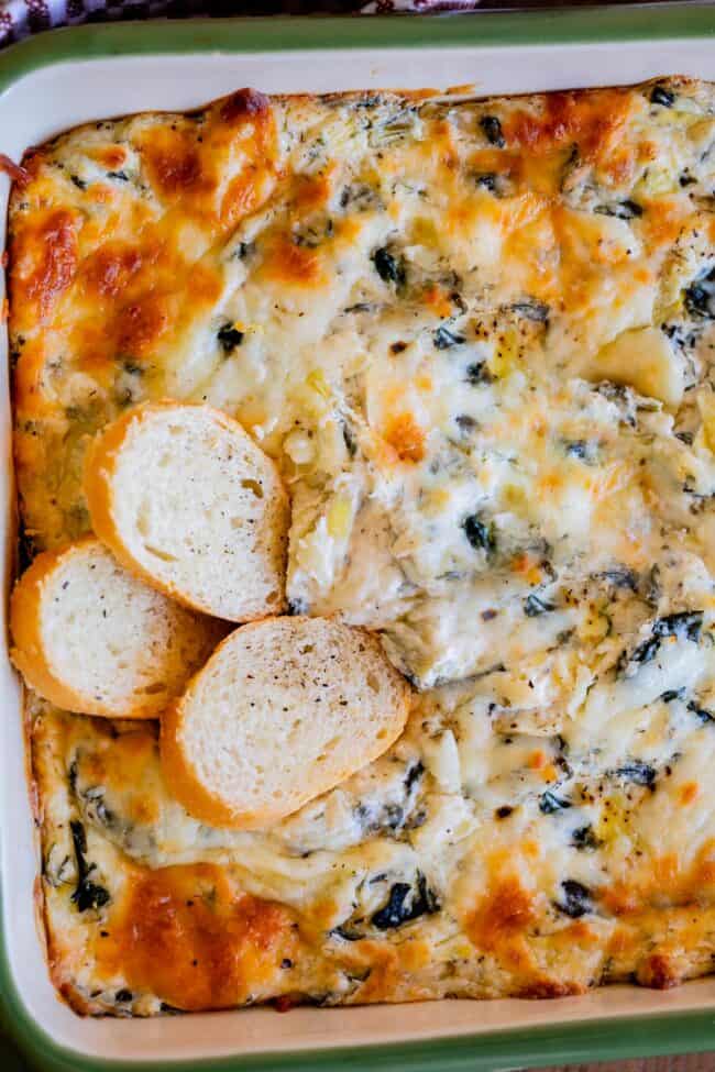 easy spinach artichoke dip in a green dish with 3 breads placed on top