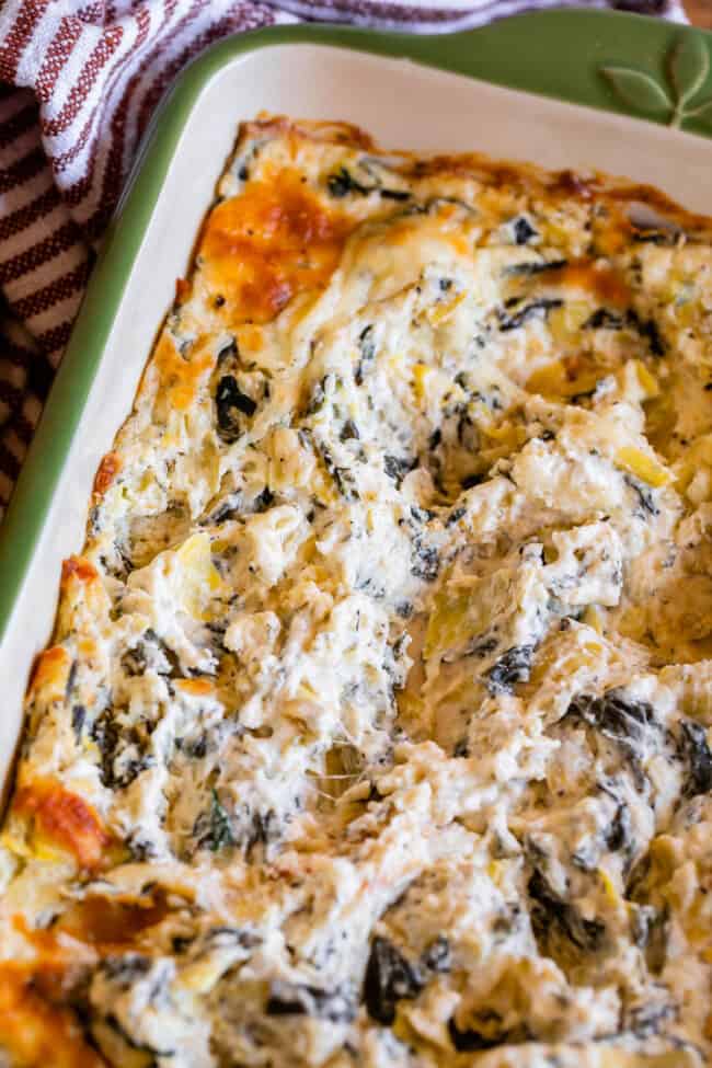 green casserole dish full of hot spinach artichoke dip, swirled
