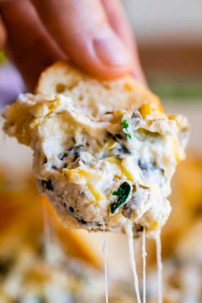 hand holding bread dipped into spinach artichoke dip recipe