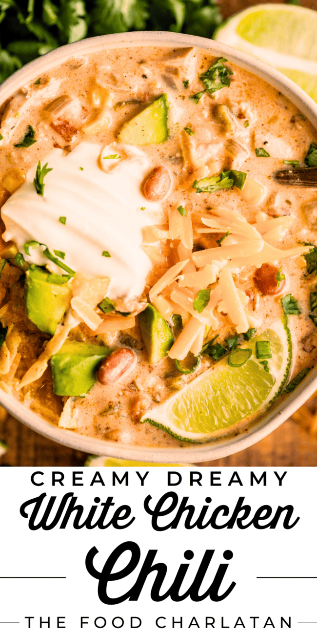 a bowl of white chicken chili with limes, avocado, and cheese.