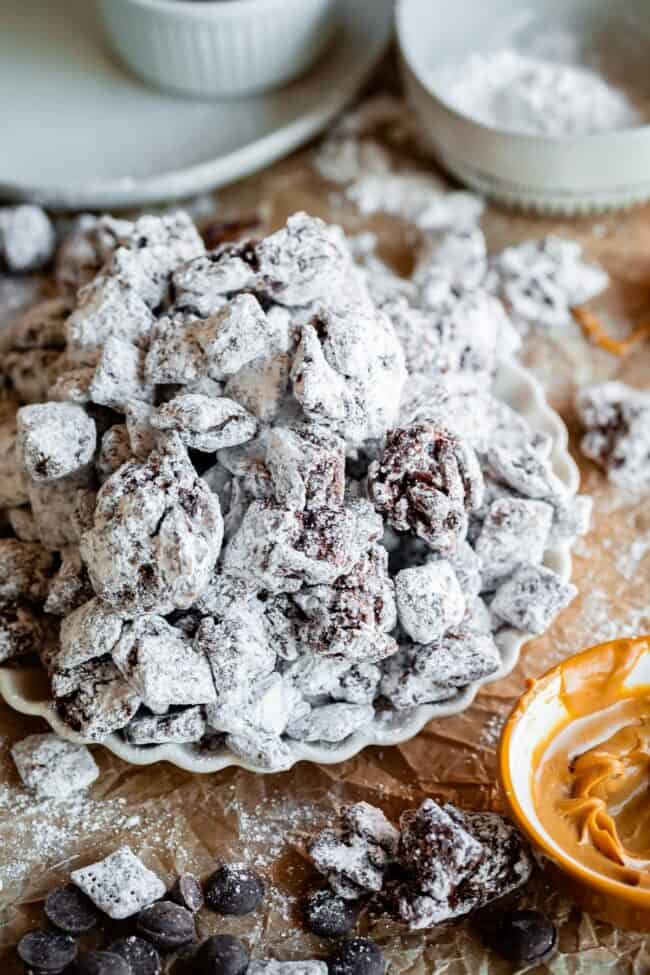 puppy chow recipe on a scallop edge plate with peanut butter in a bowl.