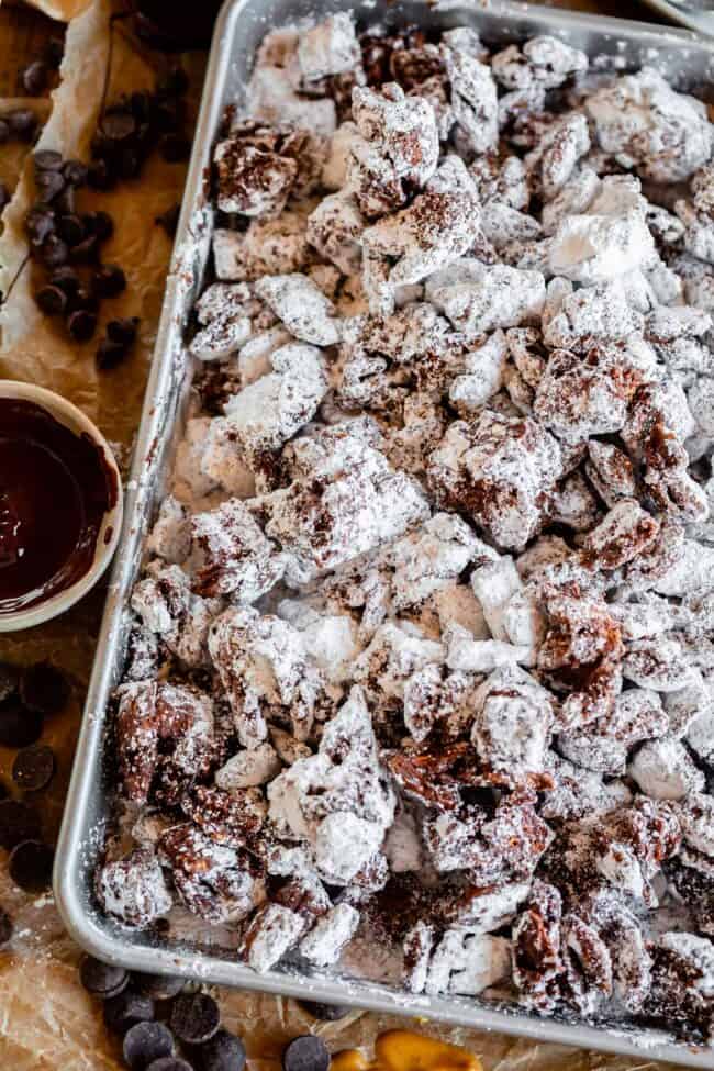 muddy buddies on a sheet pan next to a bowl of chocolate.