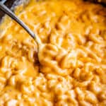 serving spoon lifting mac and cheese from a black crockpot.