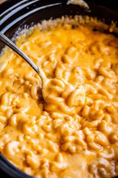 serving spoon lifting mac and cheese from a black crockpot.