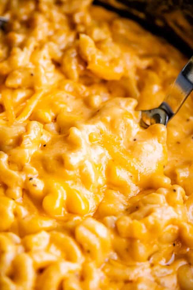 serving spoon lifting cheddar topped mac and cheese from crockpot.