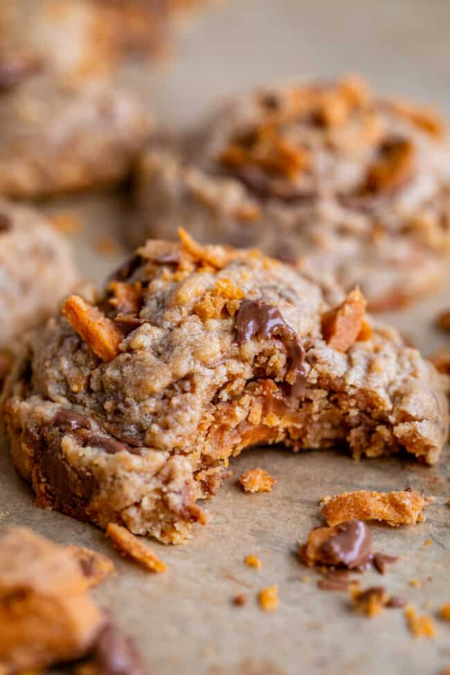 butterfinger bits cookie recipe with a bite taken out, shot from the side on parchment paper.