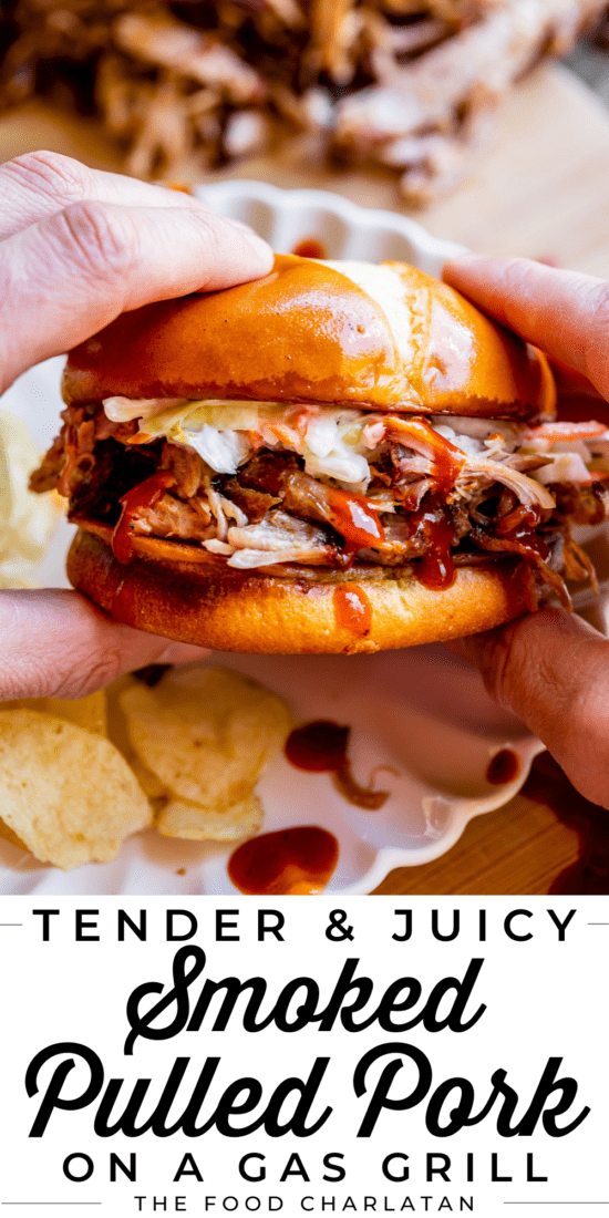 hands holding a smoked pulled pork sandwich over a white plate with chips.