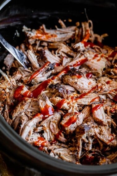 pulled pork in a black slow cooker, topped with barbecue sauce.