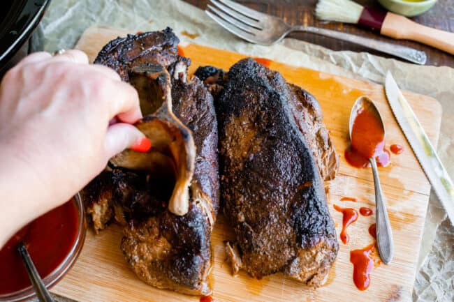 pulling the bone out of cooked pork shoulder on a cutting board.