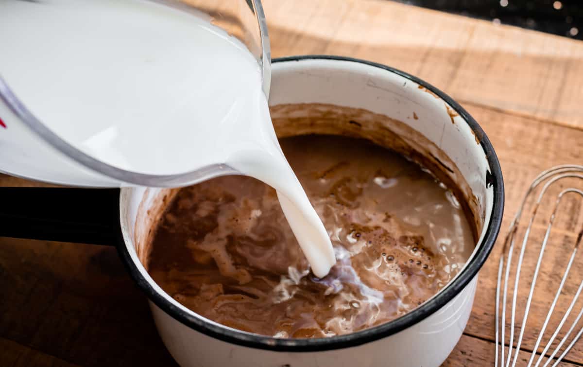 milk being poured into a white pot full of hot chocolate.