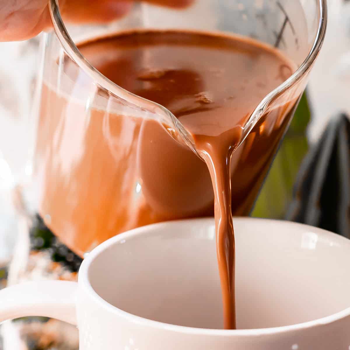 homemade hot chocolate being poured from a clear measuring cup into a white mug.