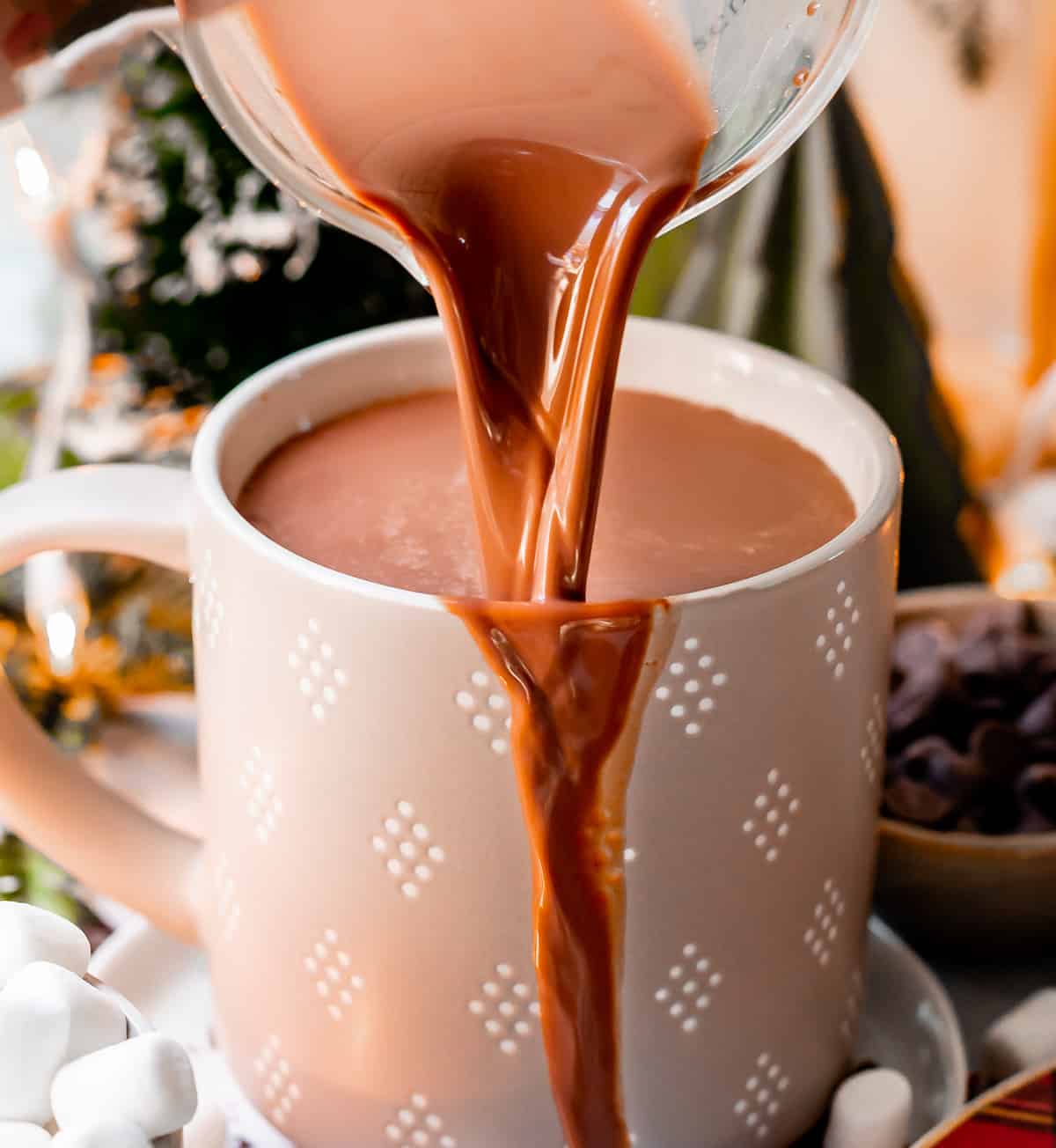 recipe for hot chocolate being poured into a gray and white mug with mini marshmallows.