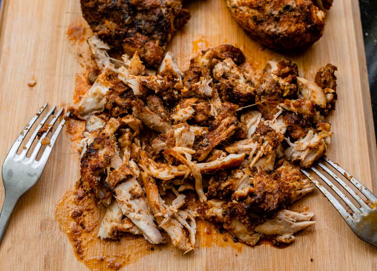 cutting board with a pile of shredded chicken and two forks on the side that did the shredding.