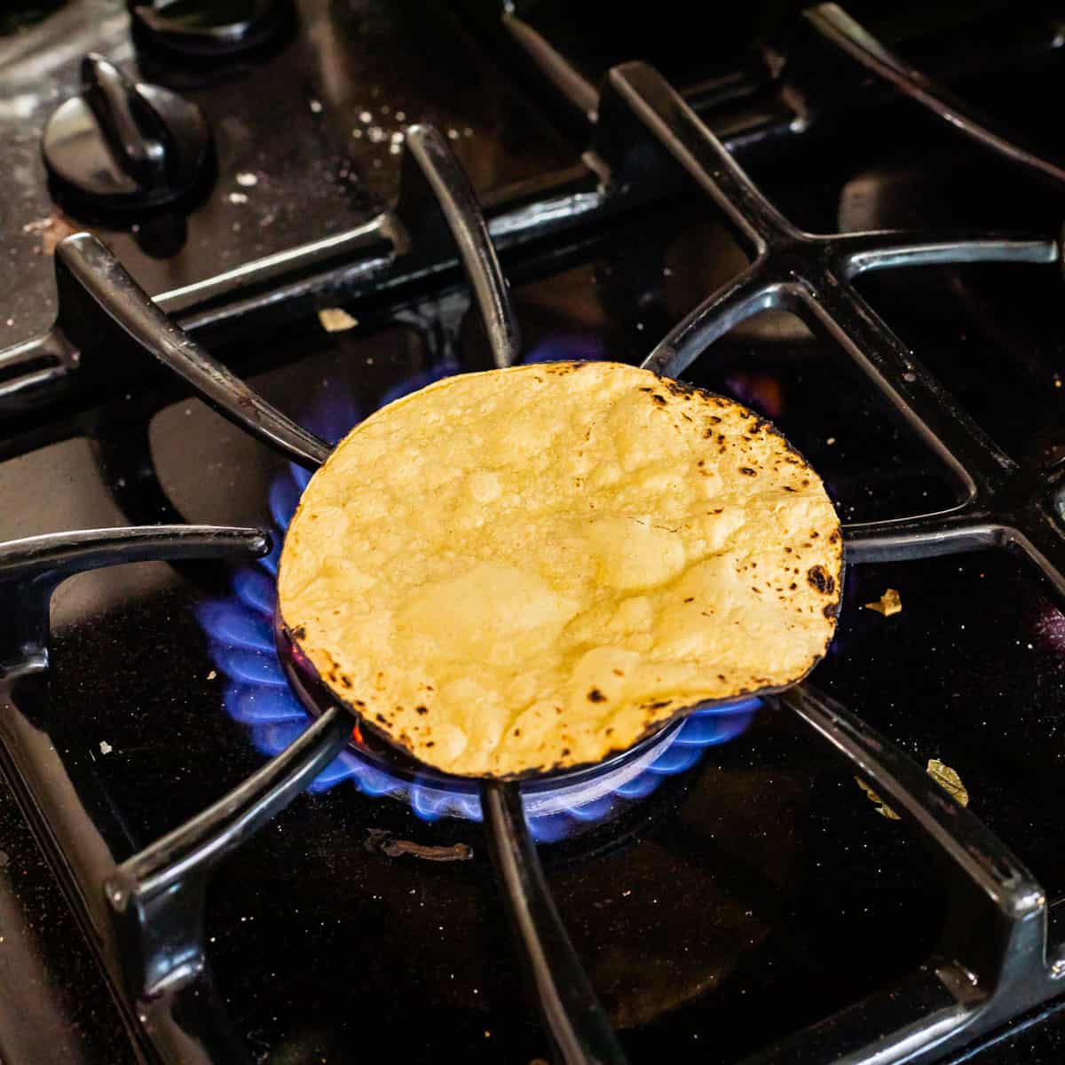 black gas stovetop with a single corn tortilla sitting over the flame to get charred.