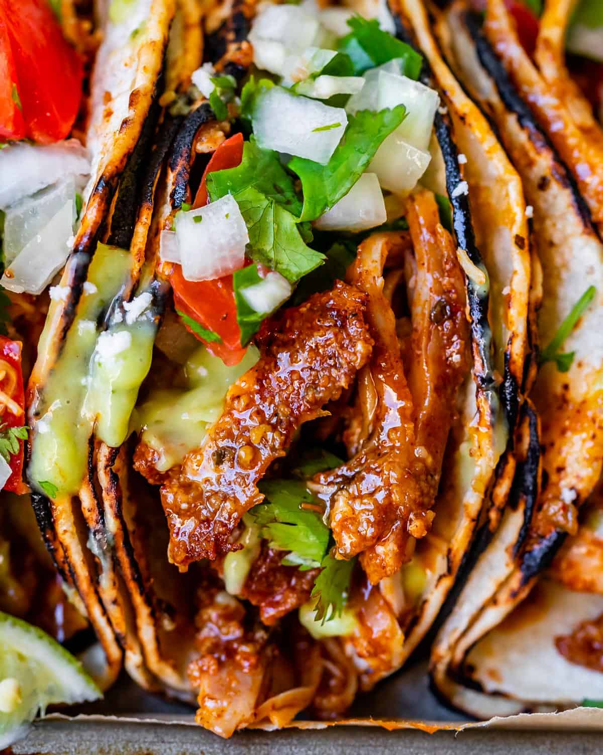 super close up of a saucy chicken piece in a taco, with onion and cilantro on top.