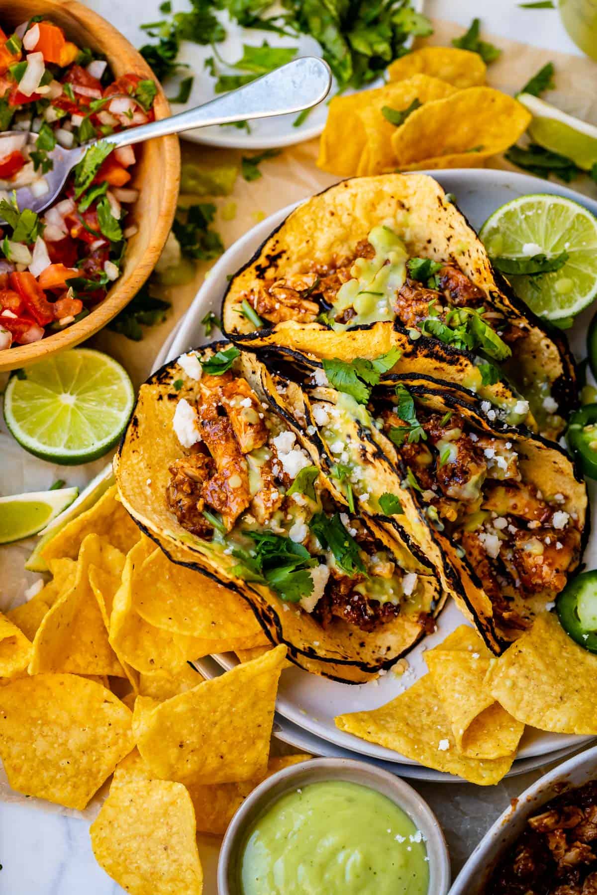 plate with three crockpot chicken tacos with garnish on top, and chips and salsa on the side.