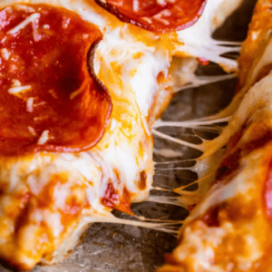 Close-up of a cheesy pepperoni pan pizza slice being pulled away, with melted cheese stretching; text at the bottom reads Pizza Hut Copycat Pan Pizza, The Food Charlatan.
