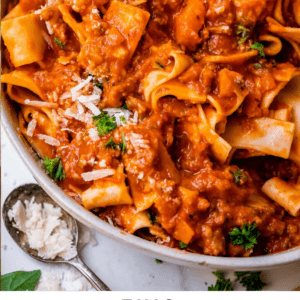white bowl of pasta mixed with red meat sauce bolognese with parmesan on the side.