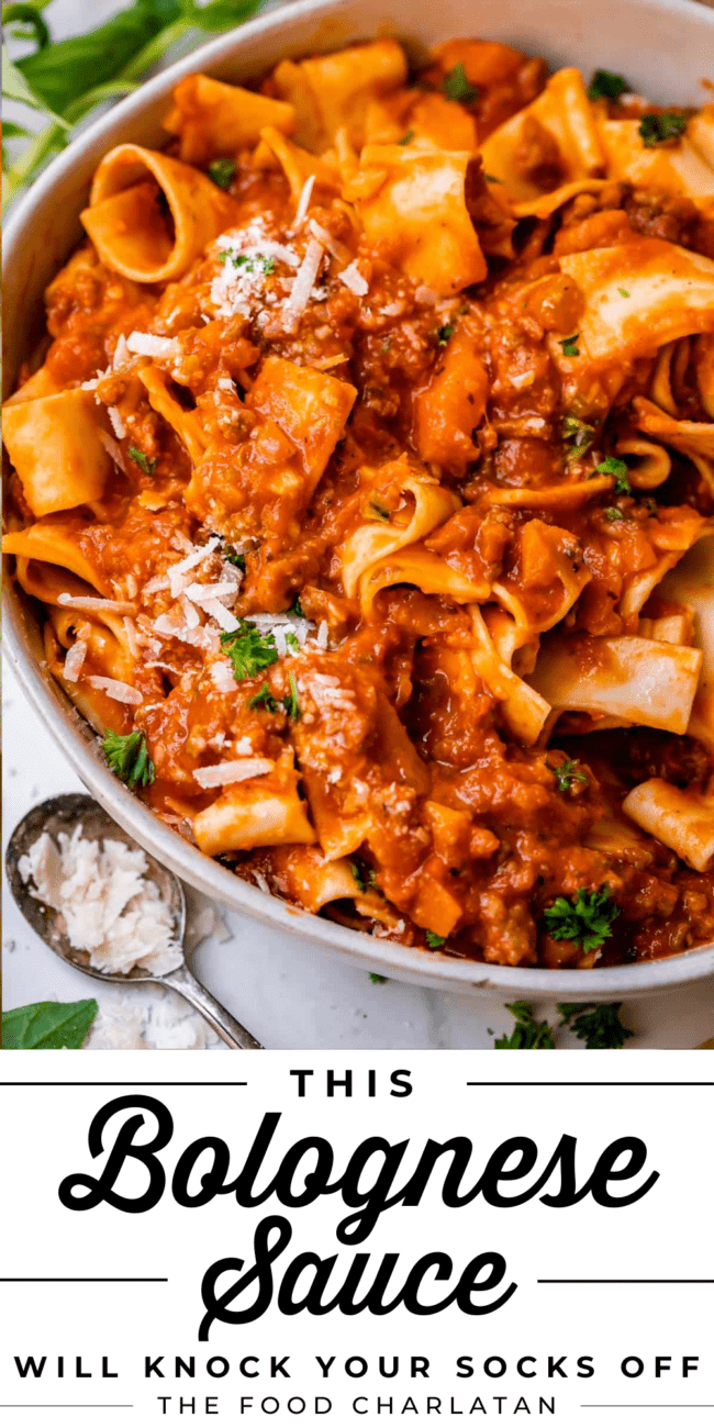 white bowl of pasta mixed with red meat sauce bolognese with parmesan on the side.