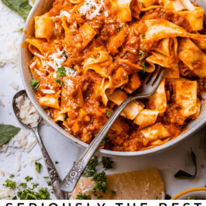 white bowl of bolognese sauce mixed with pappardelle pasta with a fork and basil garnish.