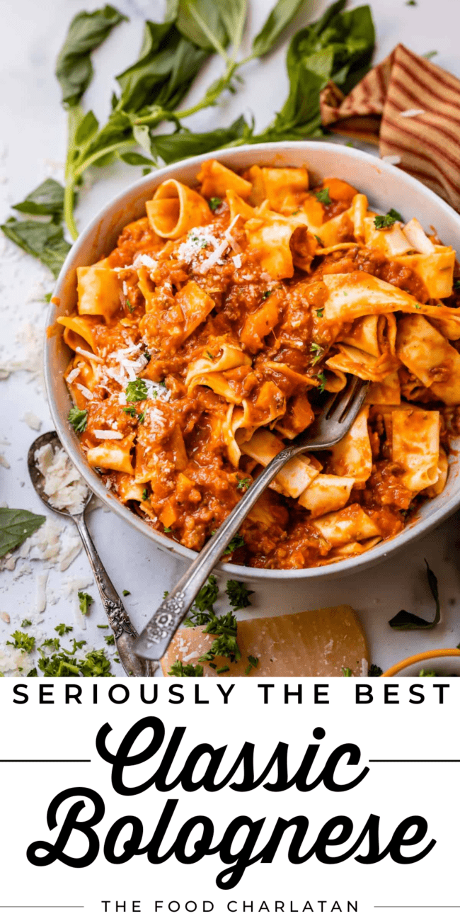 white bowl of bolognese sauce mixed with pappardelle pasta with a fork and basil garnish.