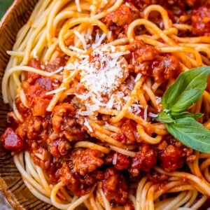 brown bowl of spaghetti noodles with easy homemade sauce on top, garnished with basil and parmesan.