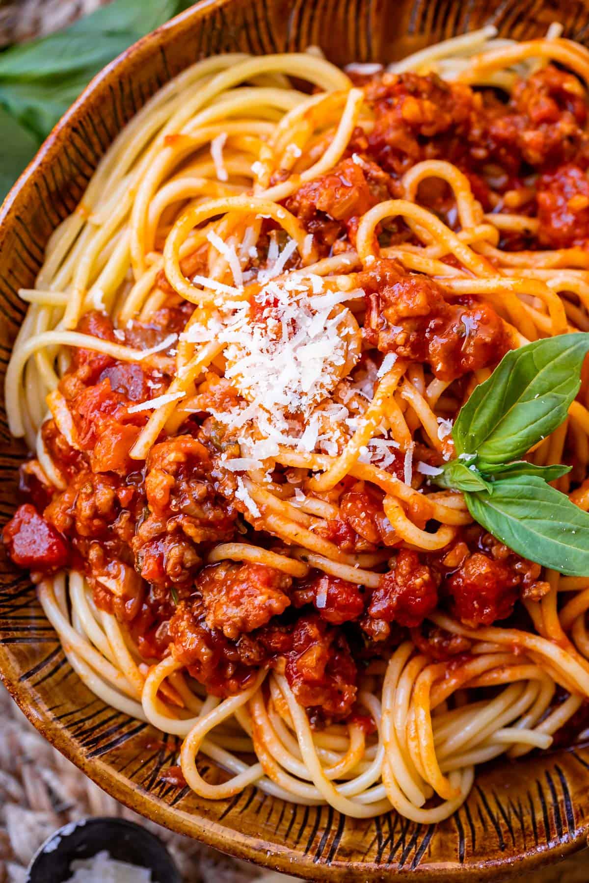 brown bowl of spaghetti noodles with easy homemade sauce on top, garnished with basil and parmesan.