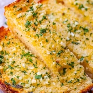 garlic bread recipe with parsley and fresh garlic on white parchment paper.