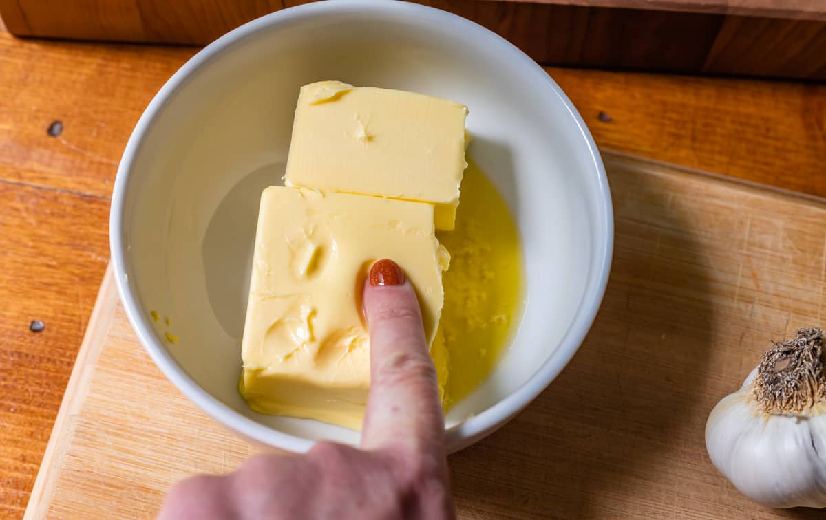 bowl with finger pushing into softened butter to show how soft the butter should be.