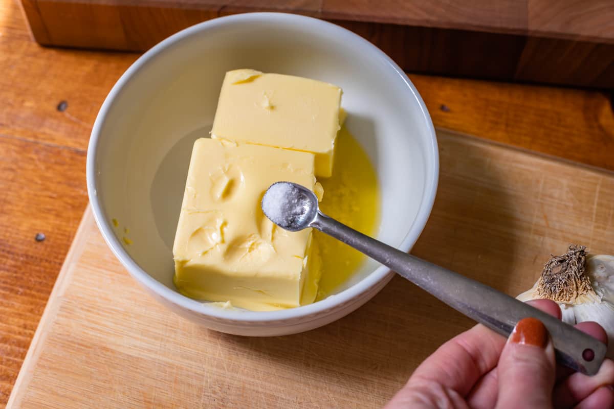 measuring spoon with salt about to be poured over softened butter in a bowl.