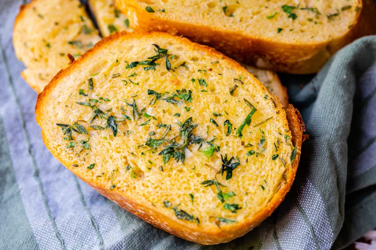 close up of a slice of baked garlic bread with melted butter, crusty edges, and soft center.
