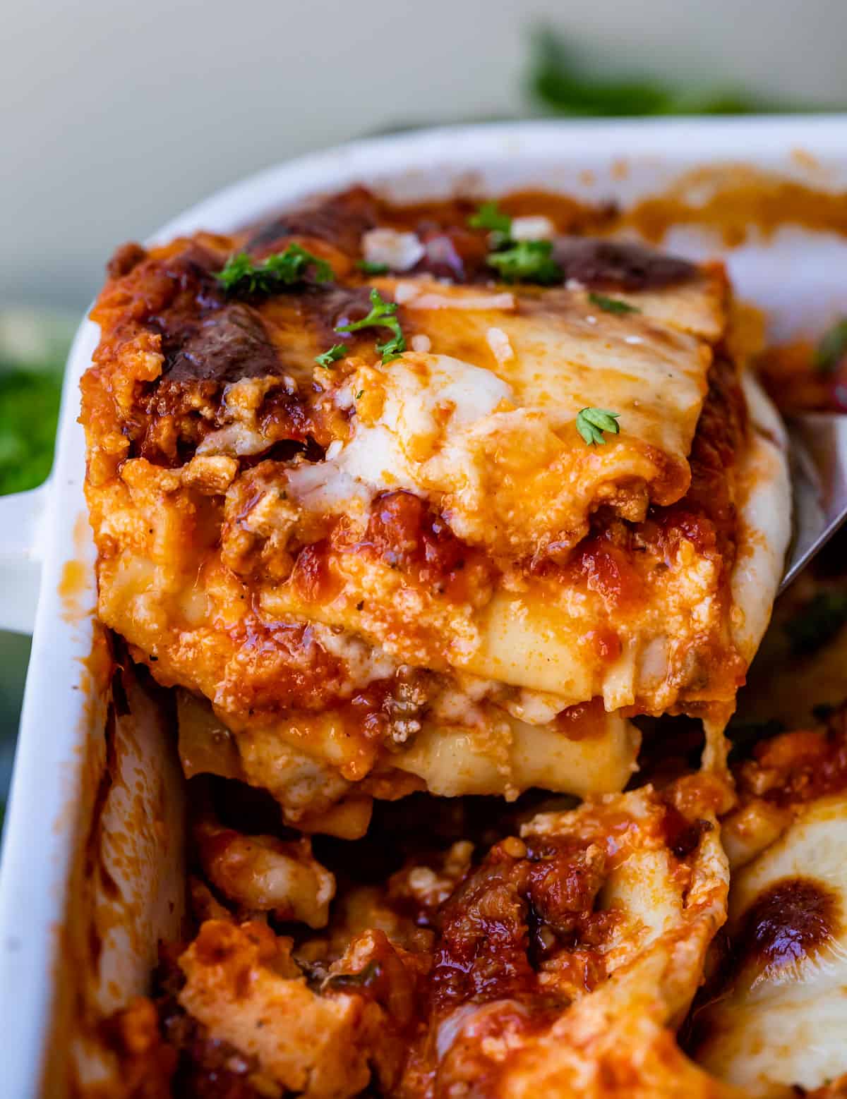 a spatula lifting a slice of lasagna out of a white casserole dish.