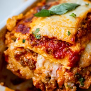 a piece of the best homemade lasagna being lifted from the white pan.