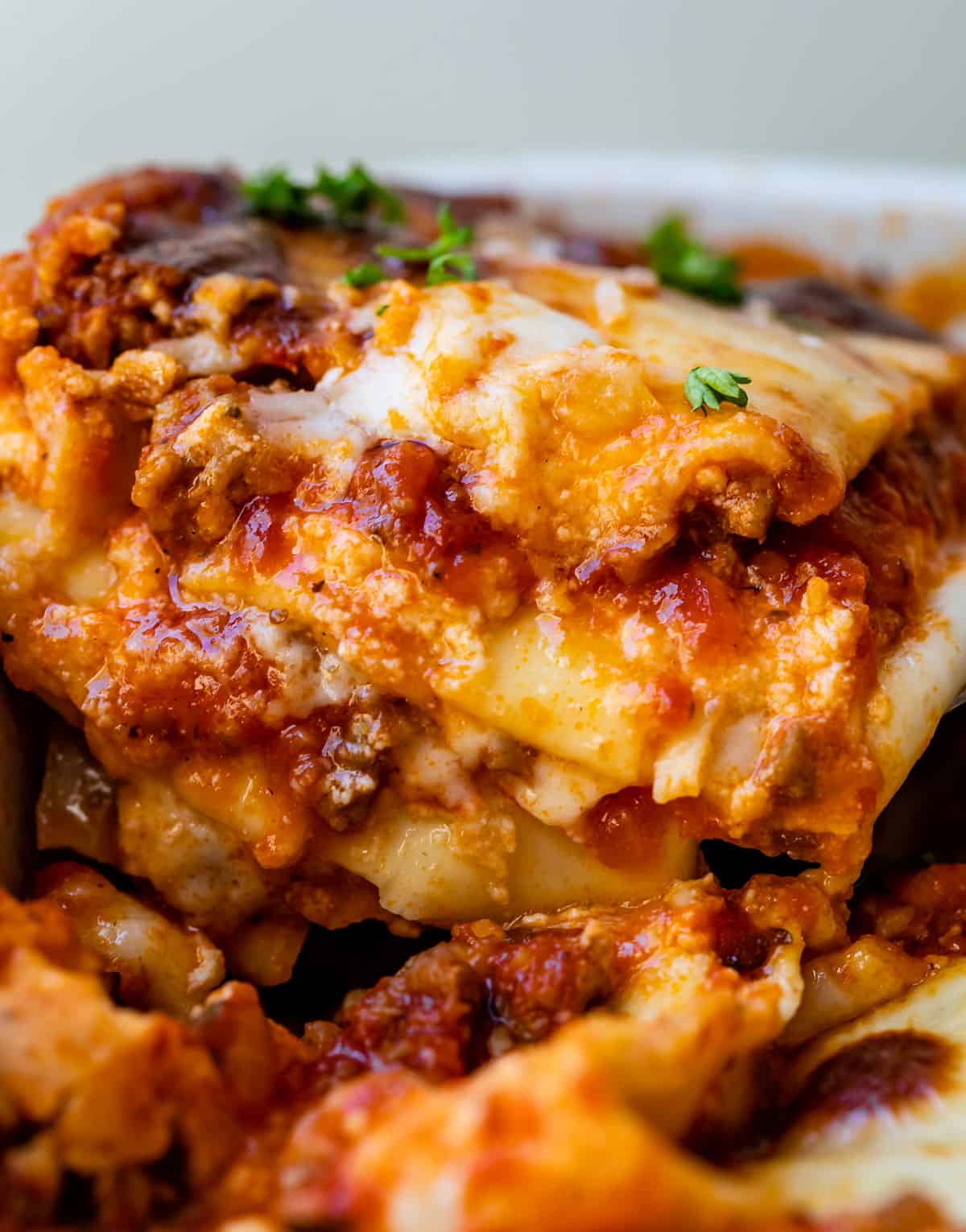 lifting a slice of the best lasagna recipe from the pan, with layers of red meat sauce and noodles.