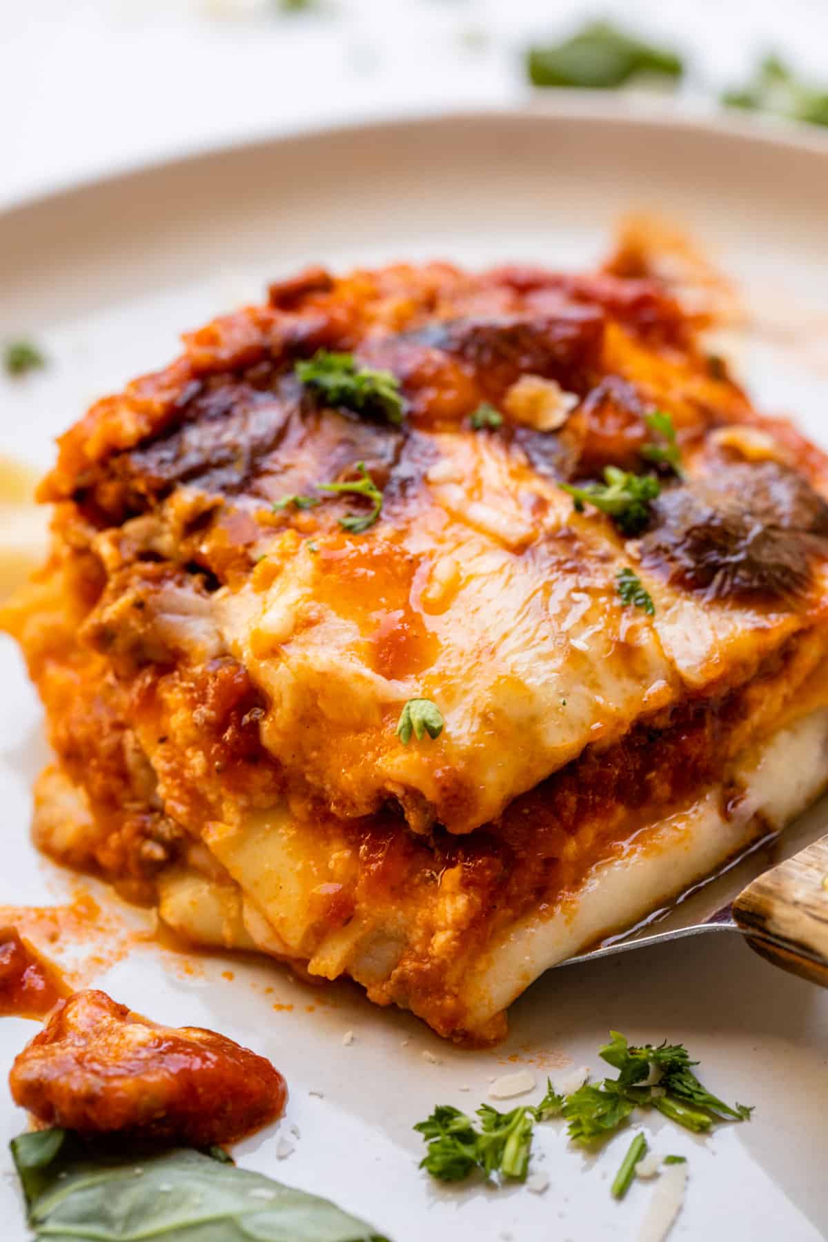 putting a piece of lasagna on a white plate with a spatula.