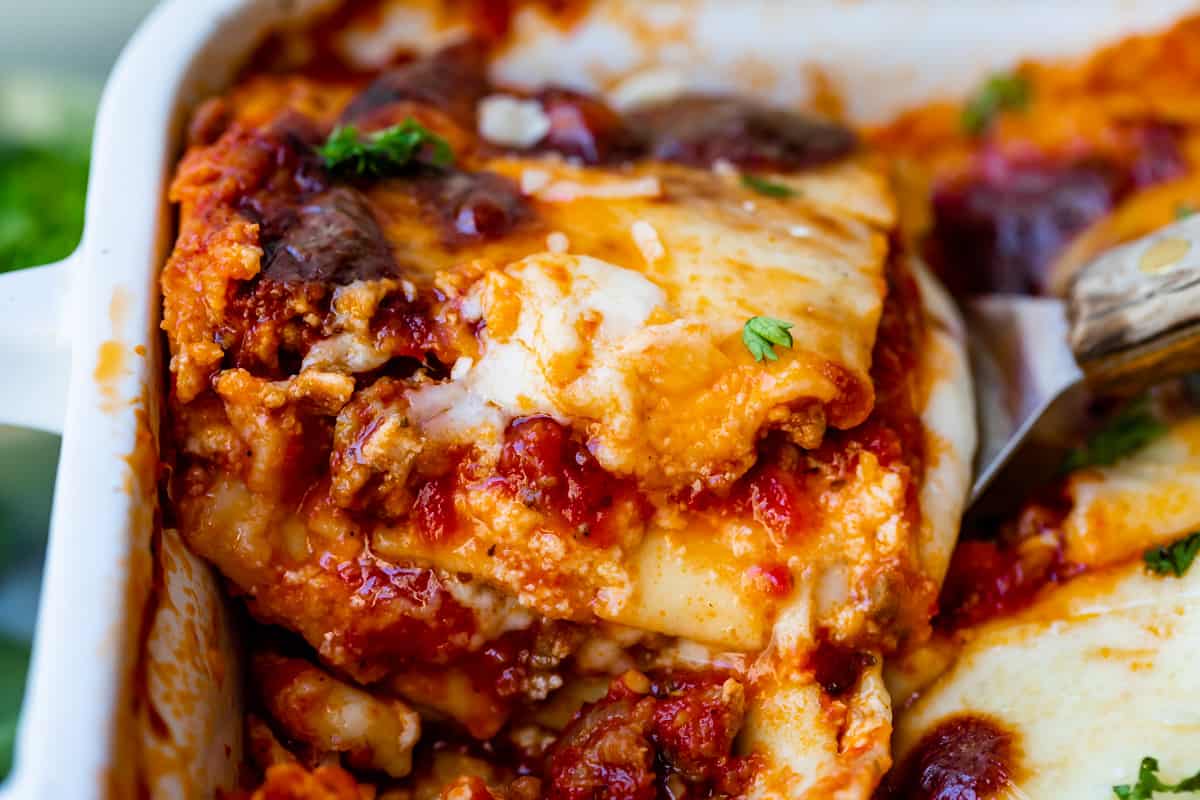 a slice of lasagna being lifted from a white pan.