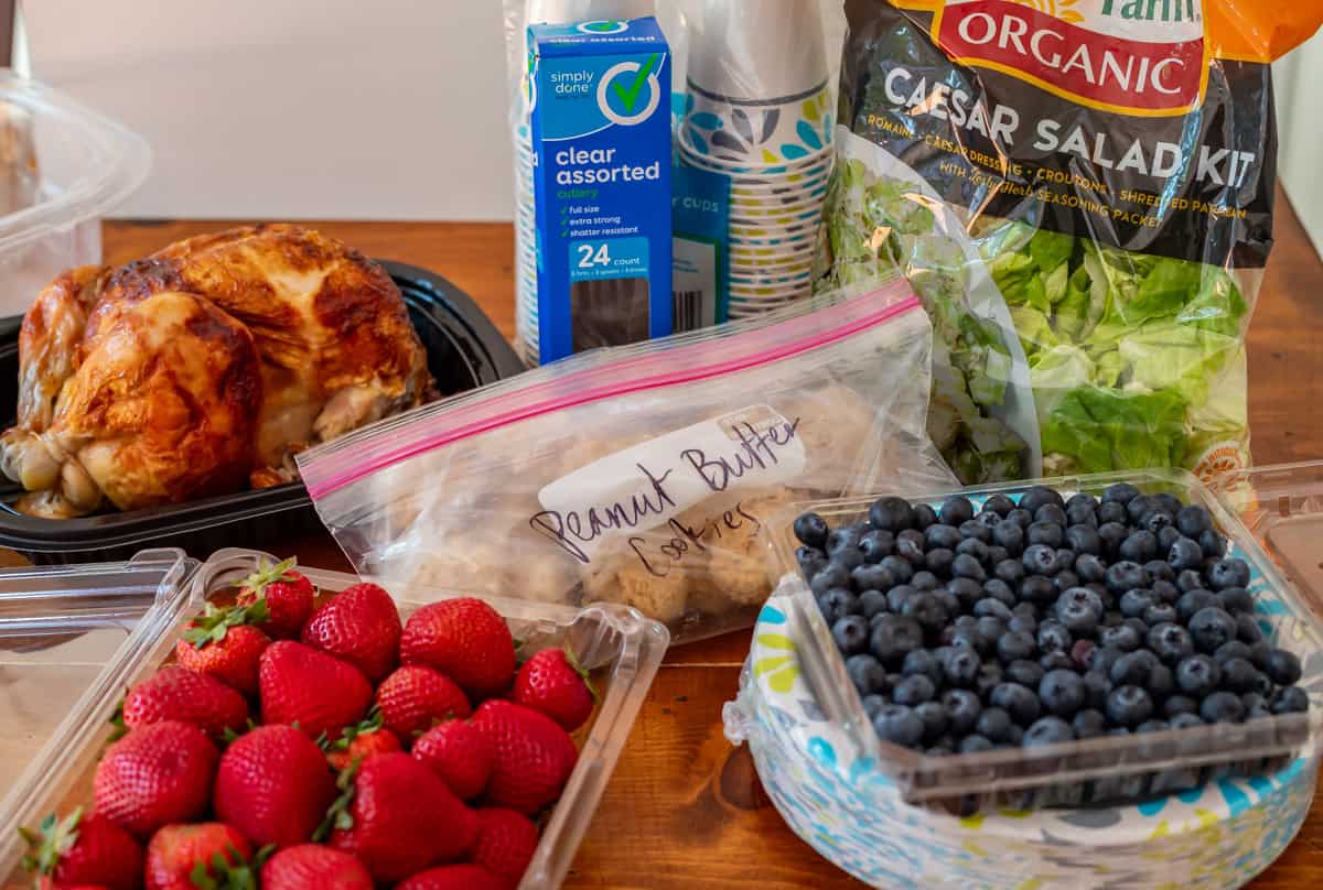 rotisserie chicken, strawberries, blueberries, salad kit, and cookie dough balls on a table.