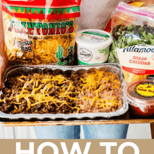 woman holding a tray of taco ingredients including taco meat and beans, chips, salsa, cheese, etc.