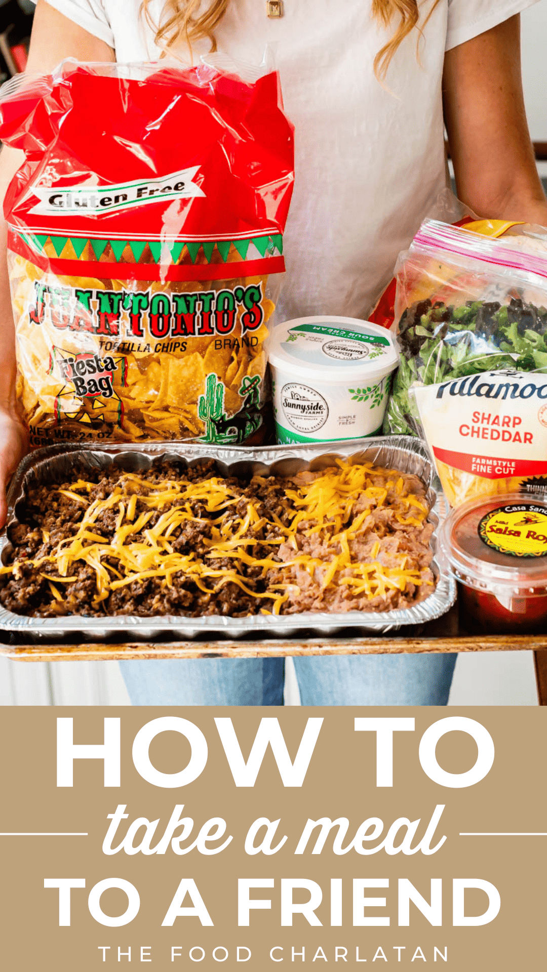 woman holding a tray of taco ingredients including taco meat and beans, chips, salsa, cheese, etc.