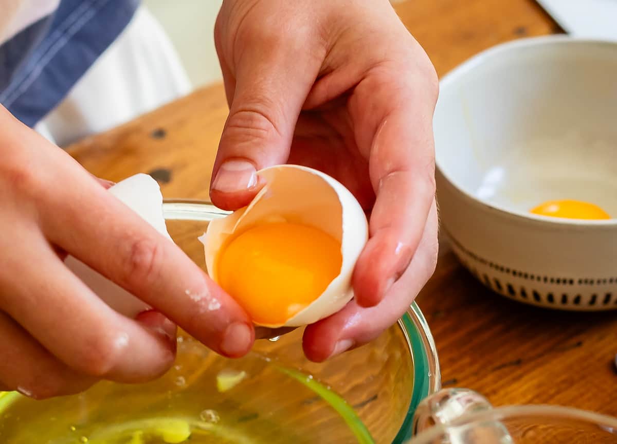 child's hands cracking an egg into a glass mixing bowl.