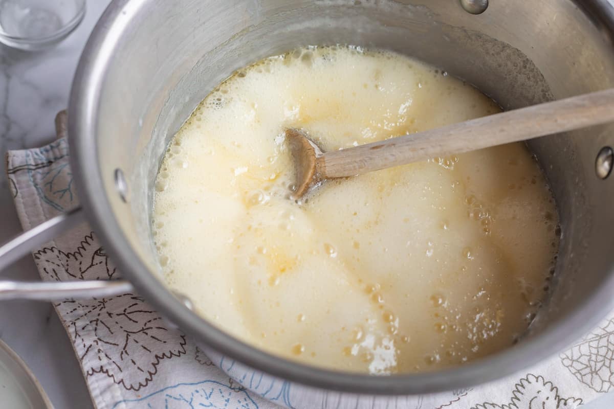 a metal pot of yellow boiling liquid with a wooden spoon.