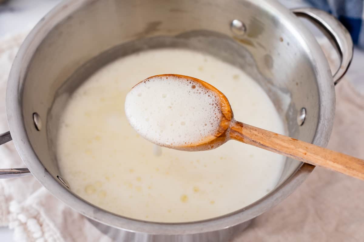 wooden spoon holding up bubbly white syrup from a metal spoon.