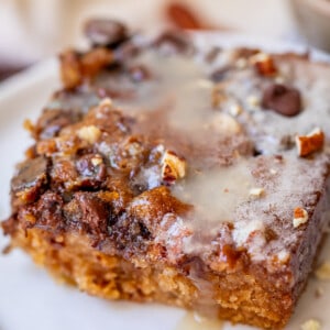 cut piece of picnic cake with drippy buttermilk glaze over crunchy topping on a white plate.
