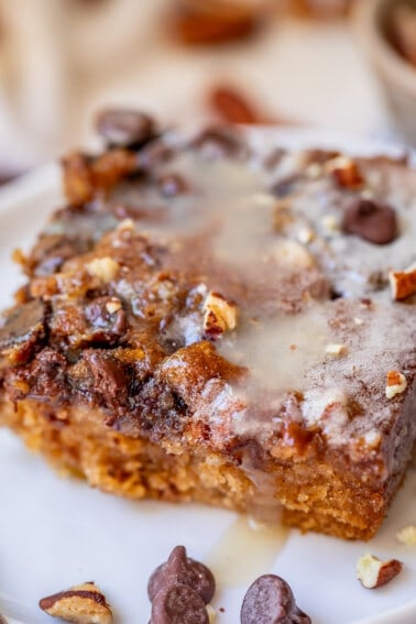 cut piece of picnic cake with drippy buttermilk glaze over crunchy topping on a white plate.